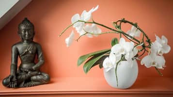 Een Boeddhabeeld en een vaas met witte orchideeën op een plank.