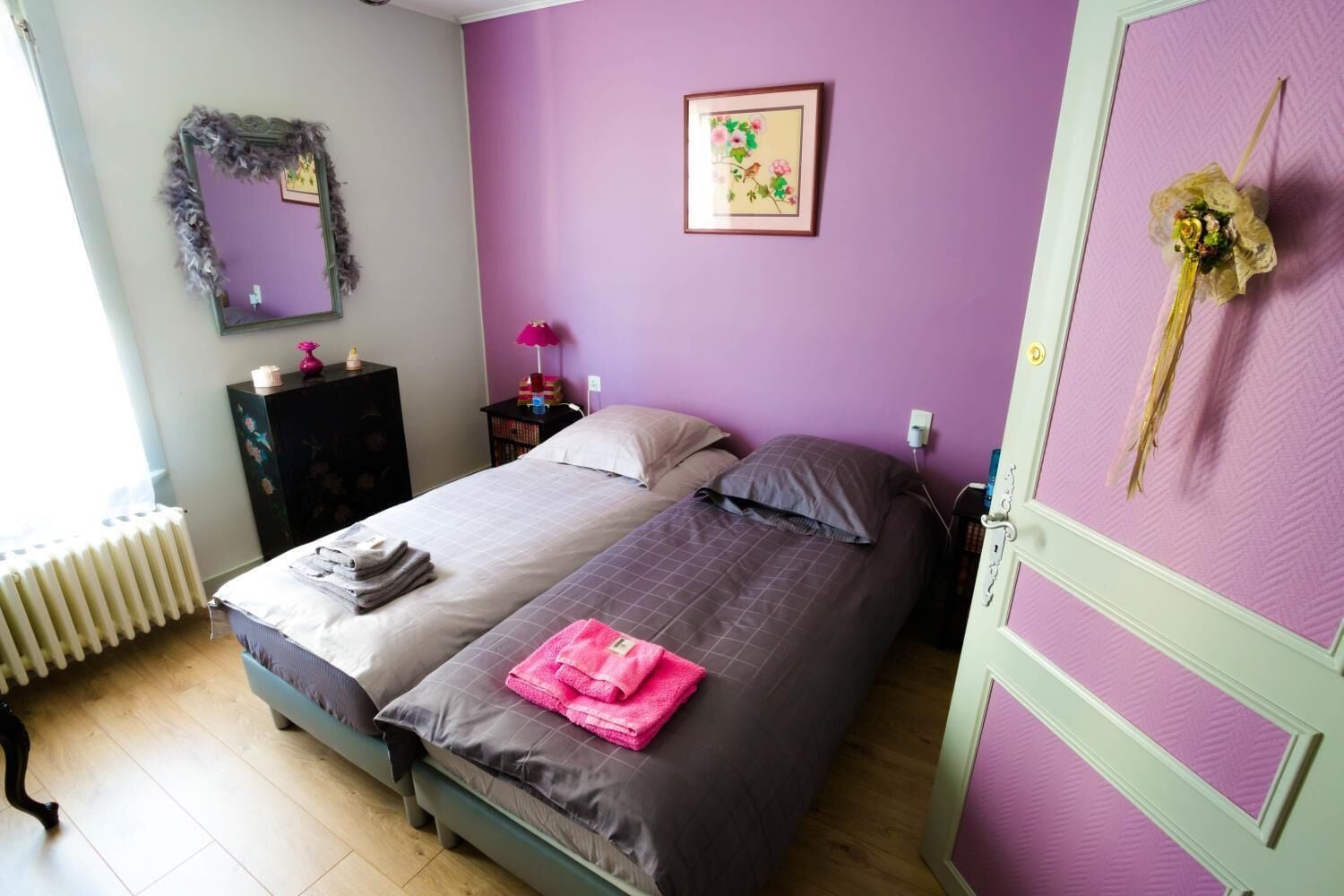 A bedroom with a bed, a dresser, a mirror, a picture on the wall, and a radiator.