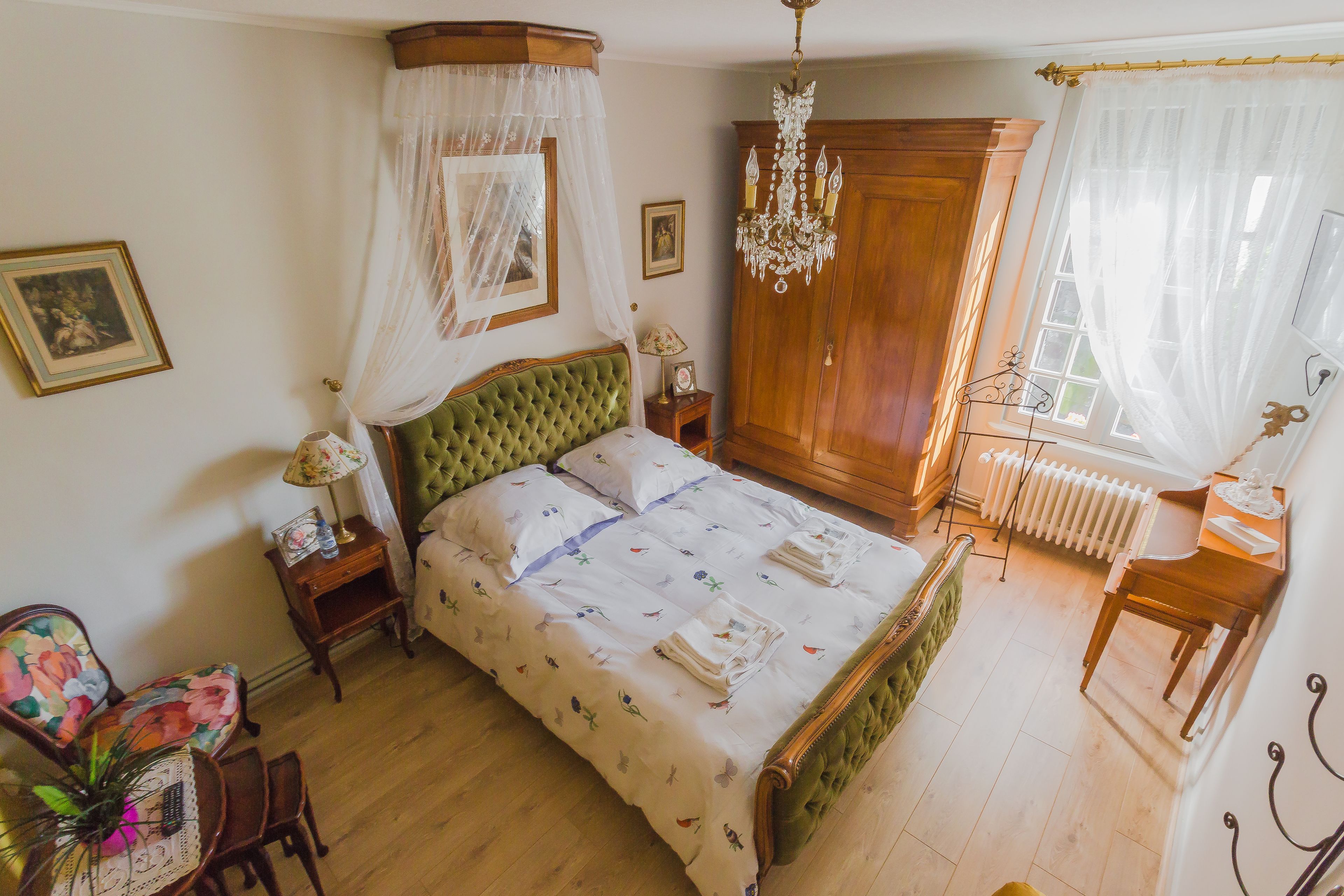 A bedroom with a four-poster bed, a wooden wardrobe, a chandelier, and a radiator.