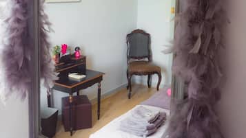 Une chambre avec un grand miroir, une chaise en bois, une petite table et un lit recouvert d’une couette blanche.