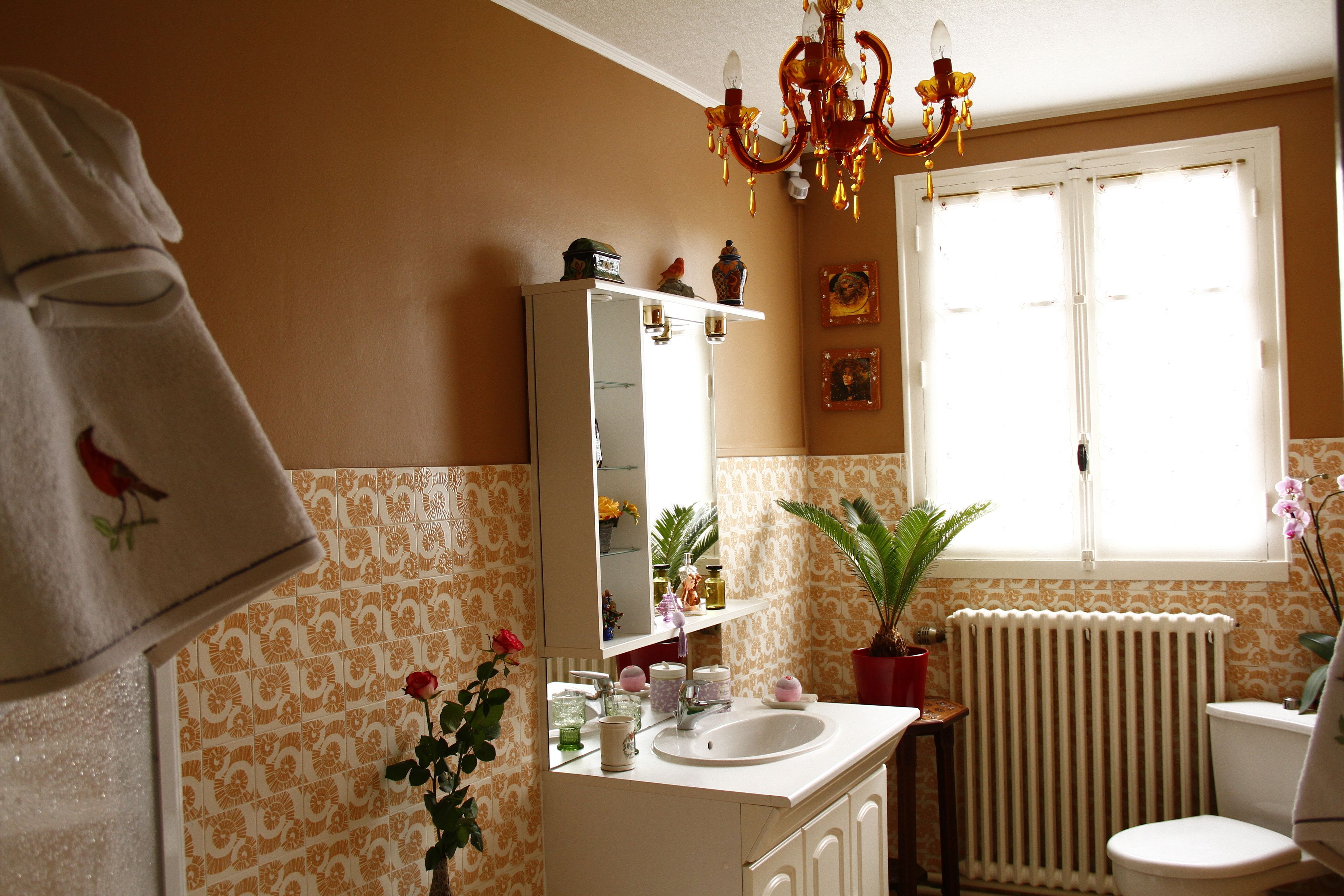 Ein Badezimmer mit weißem Waschbecken, Spiegel und Toilette, einer Topfpflanze und einem Fenster mit Jalousien.