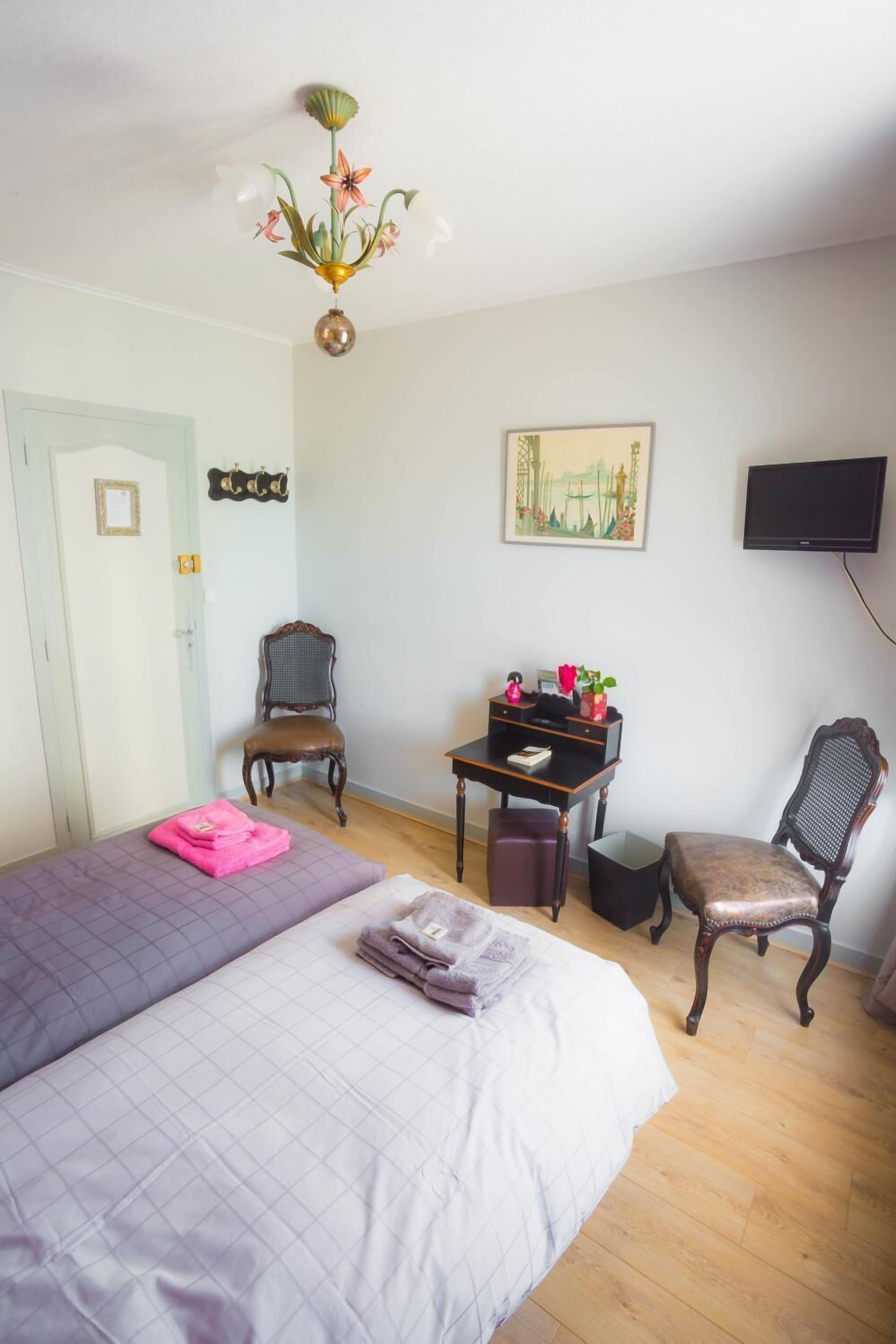 A bedroom with a bed, a desk, two chairs, a television, and a door.