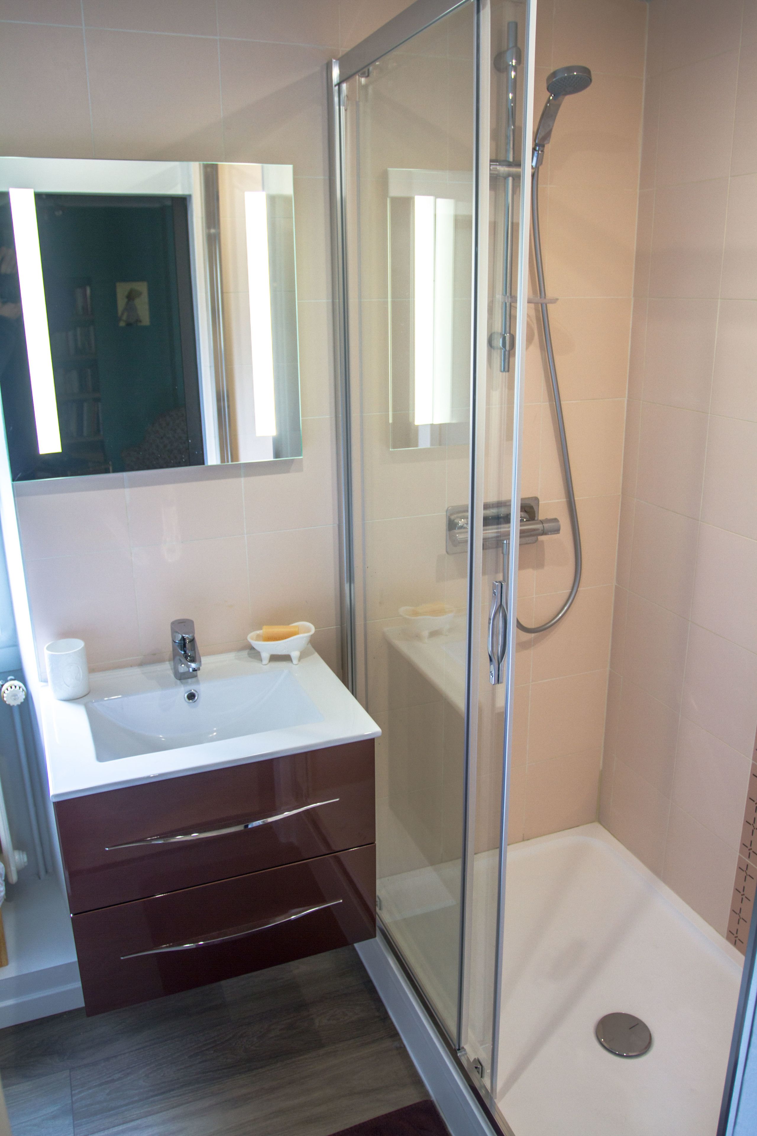 Un baño con ducha envuelta en vidrio, un lavamanos blanco y un tocador con cajones.