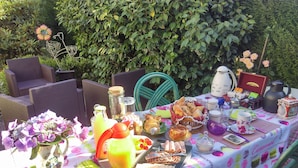 An outdoor dining setup with wicker chairs, a table covered with a patterned tablecloth, and various food and drink items.