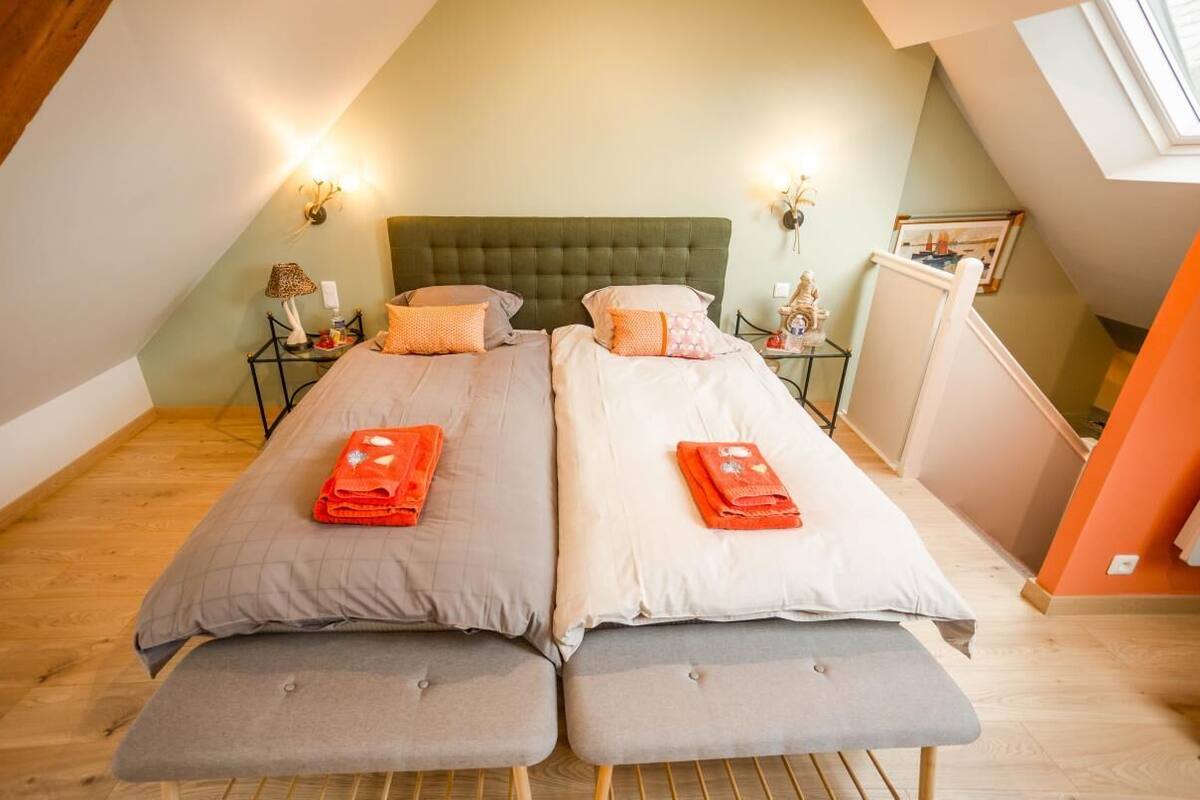 Une chambre double avec deux lits, une tête de lit verte, des lampes de chevet et une petite table avec une lampe.