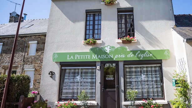 A two-story building with a sign reading "LA PETITE MAISON près de l'église".