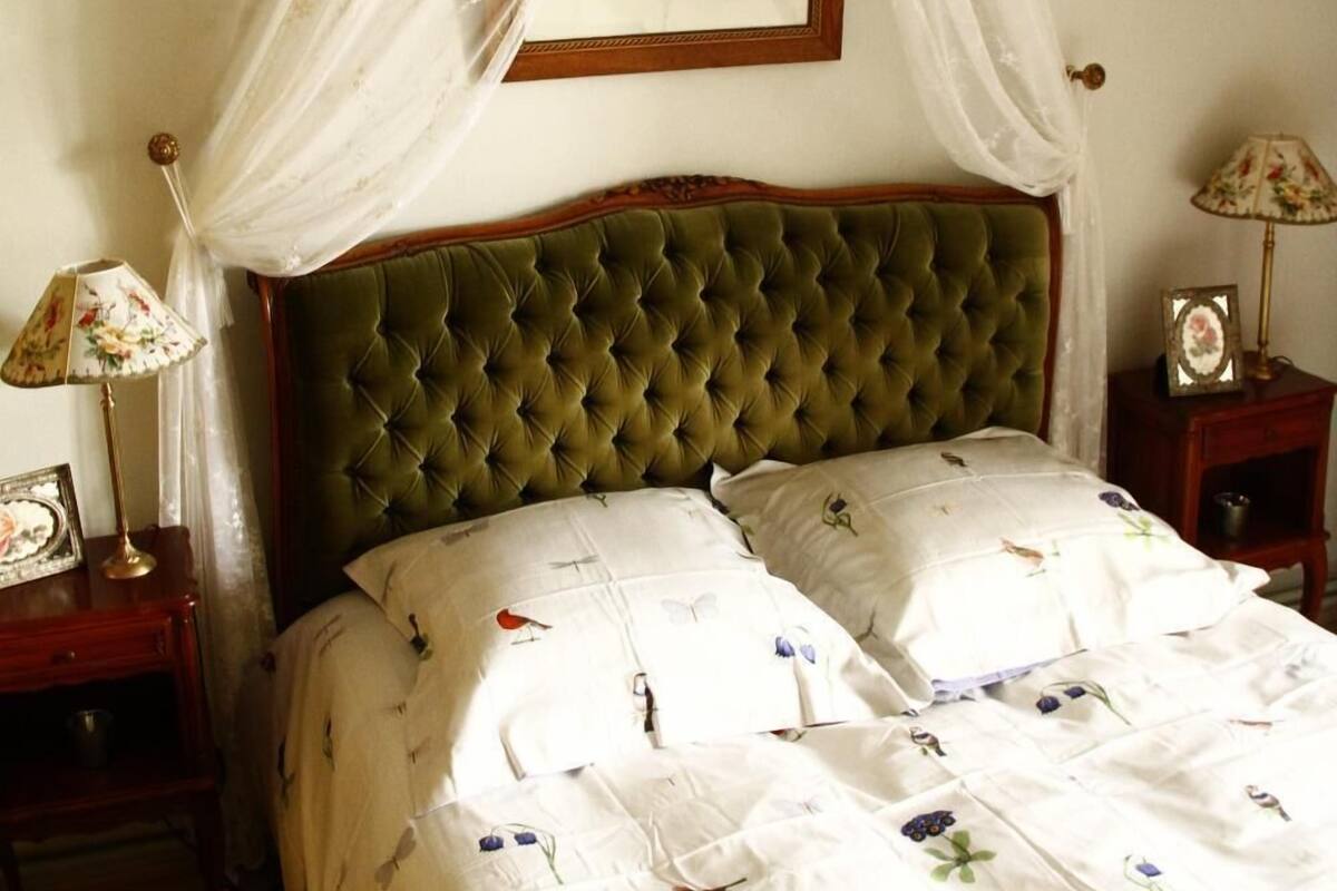 Une chambre à coucher avec un lit à baldaquin, un tableau encadré au-dessus du lit, un lustre et des tables de chevet avec des lampes.