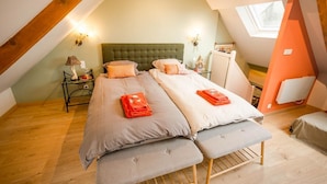 A cozy attic bedroom with two beds, a skylight, and a small table with a lamp.