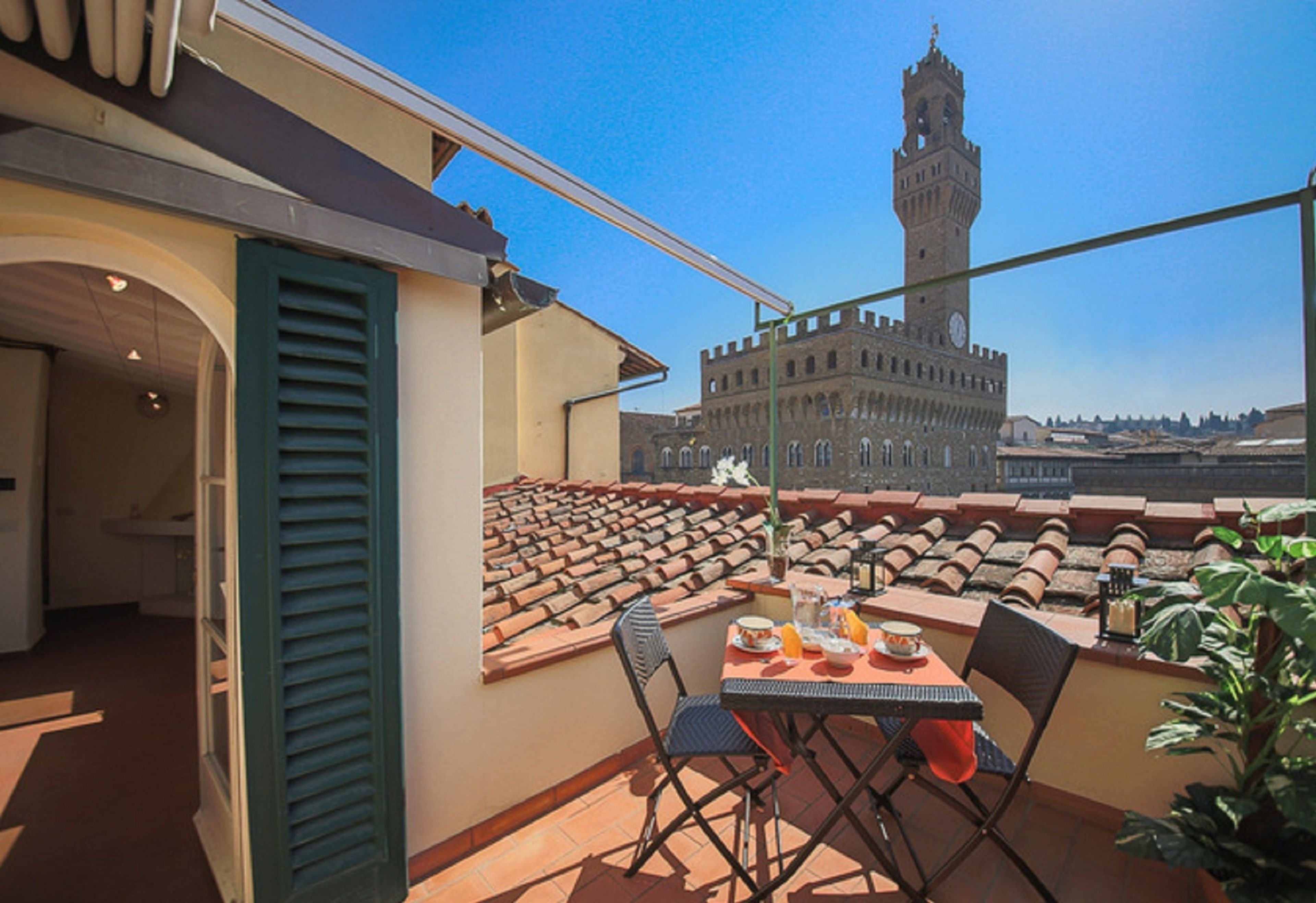 A rooftop terrace with a table set for dining, overlooking a historic tower.