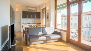Ein modernes Wohnzimmer mit einer Couch, einem Flachbildfernseher und einem Balkon mit Blick auf Gebäude.