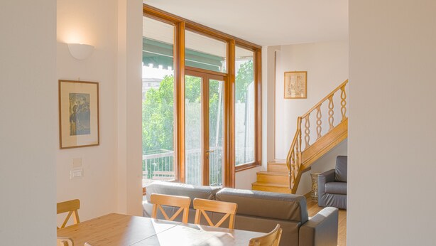 Ein Essbereich mit Holztisch und -stühlen, einer Couch und einer Treppe mit Holzbalkonen.