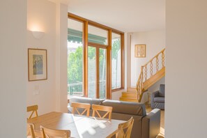 Un comedor con una mesa y sillas de madera, un sofá y una escalera con barandilla de madera.