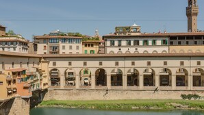 A historic building with arched windows and a tower, located beside a river. - Ponte Vecchio Balcony (Florence)
