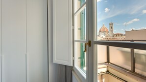 Una habitación con un ventanal grande, un armario blanco y vistas a un edificio histórico con cúpula y torre.