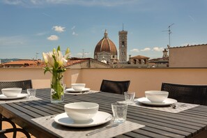 A dining table set with white bowls, plates, and glasses, with a vase of flowers in the center. In the background, there is a view of a historic building with a dome and a bell tower. - Rondinelli Terrace (Florence)