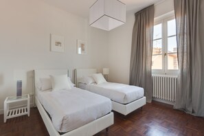A hotel room with two beds, a small bedside table, a lamp, a window with curtains, and a radiator. - Rondinelli Terrace (Florence)