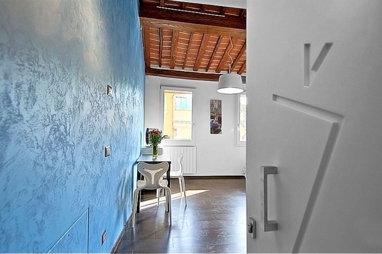Un couloir avec un mur bleu, un plafond en bois et une porte blanche.