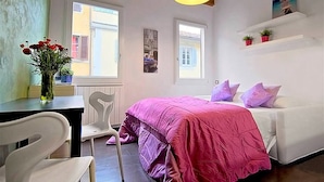 A bedroom with a bed, a desk with a vase of flowers, and two windows. - San Gallo Suites III (Florence)