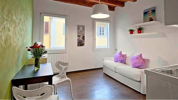 A room with a wooden ceiling, white walls, a white sofa with purple pillows, a dining table with chairs, and a vase with flowers. - San Gallo Suites III (Florence)