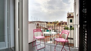 A balcony with two pink chairs and a small table, overlooking a cityscape with buildings and a cloudy sky. - San Gallo Suites IV (Florence)