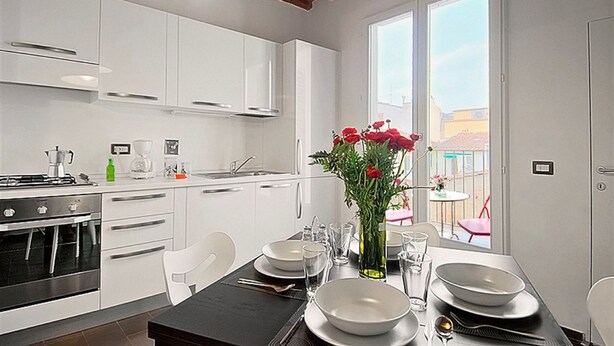 A modern kitchen with white cabinets, a dining table set for four, and a large window offering a view of the outside. - San Gallo Suites IV (Florence)