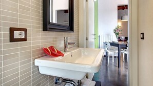 A bathroom with a white sink, a mirror, and a towel rack. There is a dining area visible in the background with a table and chairs. - San Gallo Suites IV (Florence)