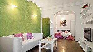 A modern living room with a white sofa, a small white table, and a bed with pink bedding. - San Gallo Suites IV (Florence)