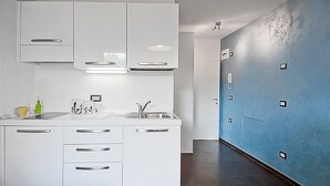 A modern kitchen with white cabinets, a sink, and a countertop. There are cabinets above the countertop and a blue wall with a door on the right. - San Gallo Suites V (Florence)