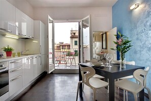 A modern kitchen with white cabinets, a dining area with a dark table, and a view of the outside balcony. - San Gallo Suites VI (Florence)