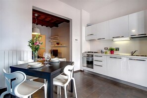 A modern kitchen with white cabinets, a dark countertop, and a dining area with white chairs and a table. - San Gallo Suites VI (Florence)