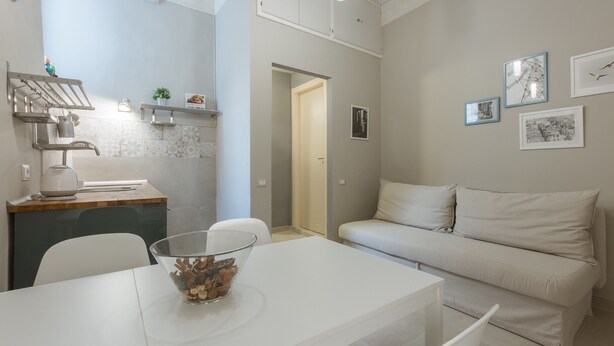 A modern kitchen with a dining table, a bowl of fruit, and a white sofa in the living area. - San Lorenzo Chic (Florence)