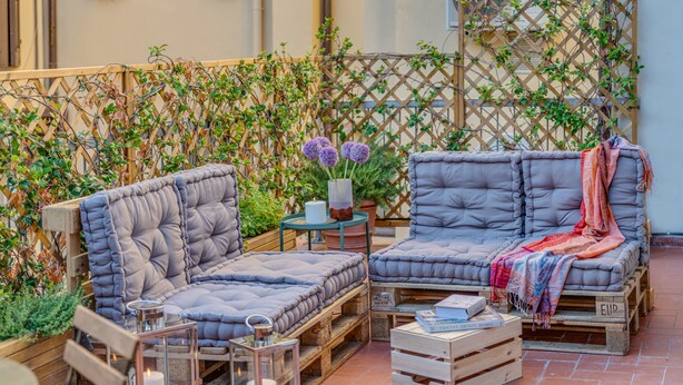 A cozy outdoor seating area with cushioned sofas and a small table, surrounded by potted plants and a wooden fence. - San Lorenzo Terrace (Florence)