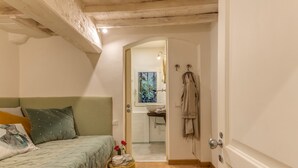 A bedroom with a bed, a bedside table with a vase and a cup, and a view into the bathroom through an open door. - San Lorenzo Terrace (Florence)