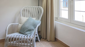 A room with a white wicker chair, a floor lamp, and a window with curtains. - San Marco Suite III (Florence)