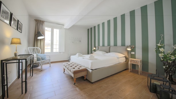 A bedroom with a bed, a desk, a chair, a window, and a striped wall. - San Marco Suite III (Florence)