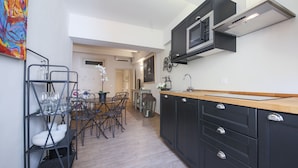 A modern kitchen with black cabinets, a wooden countertop, and a built-in microwave. There is a dining area with a table and chairs, and a small island with a sink. - San Marco Suite III (Florence)