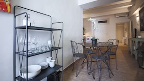 A dining area with a metal shelving unit holding plates, bowls, and glasses. There is a round table with chairs and a potted plant. - San Marco Suite III (Florence)