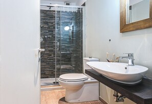 A modern bathroom with a glass shower enclosure, a white toilet, and a large vessel sink.