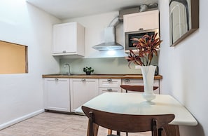 A small kitchen with white cabinets, a stainless steel range hood, a sink, and a vase with flowers on the counter.