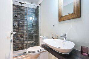 Une salle de bain moderne avec une douche Ă parois de verre, des toilettes blanches et un grand lavabo surmontĂ© dâun miroir.