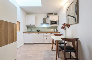 A compact kitchen with white cabinets, a microwave, a kettle, and a dining area with a table and chairs.