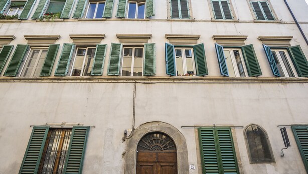 A building facade with multiple windows, some with green shutters, and a central arched doorway. - Sant’Ambrogio Passion (Florence)