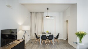 A modern dining area with a TV, dining table, chairs, and a small side table with a vase. - Sant’Ambrogio Passion (Florence)