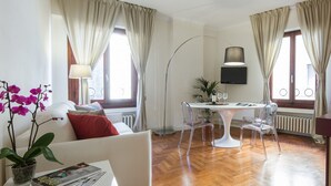 A modern living room with a round dining table, clear chairs, a sofa with red cushions, a floor lamp, and a potted plant. - Santa Maria View (Florence)
