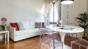 A modern living room with a white sofa, clear chairs, a round dining table, and a large floor lamp. - Santa Maria View (Florence)