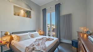 Een moderne slaapkamer met een groot bed, een nachtkastje, een dressoir en uitzicht op de stad door het raam.