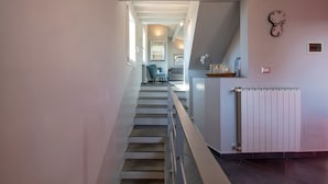 Een trap leidt naar een woonruimte met een radiator, een klok en uitzicht op een eethoek.