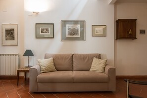 A living room with a beige sofa, a small table with a lamp, and three framed artworks on the wall. - Santo Spirito Charme (Florence)