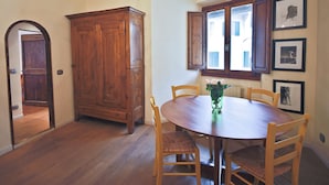 Un comedor con una mesa y sillas de madera, un armario y una ventana con contraventanas abiertas.