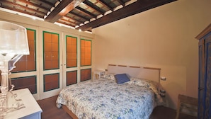 Un dormitorio con colcha estampada, vigas de madera en el techo y una mesita de noche con lámpara.